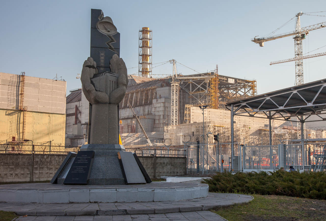 Monument dedicated to those who died during Chernobyl accident. Chernobyl reactor 4 in the background with sarcophagus falling apart behind it.